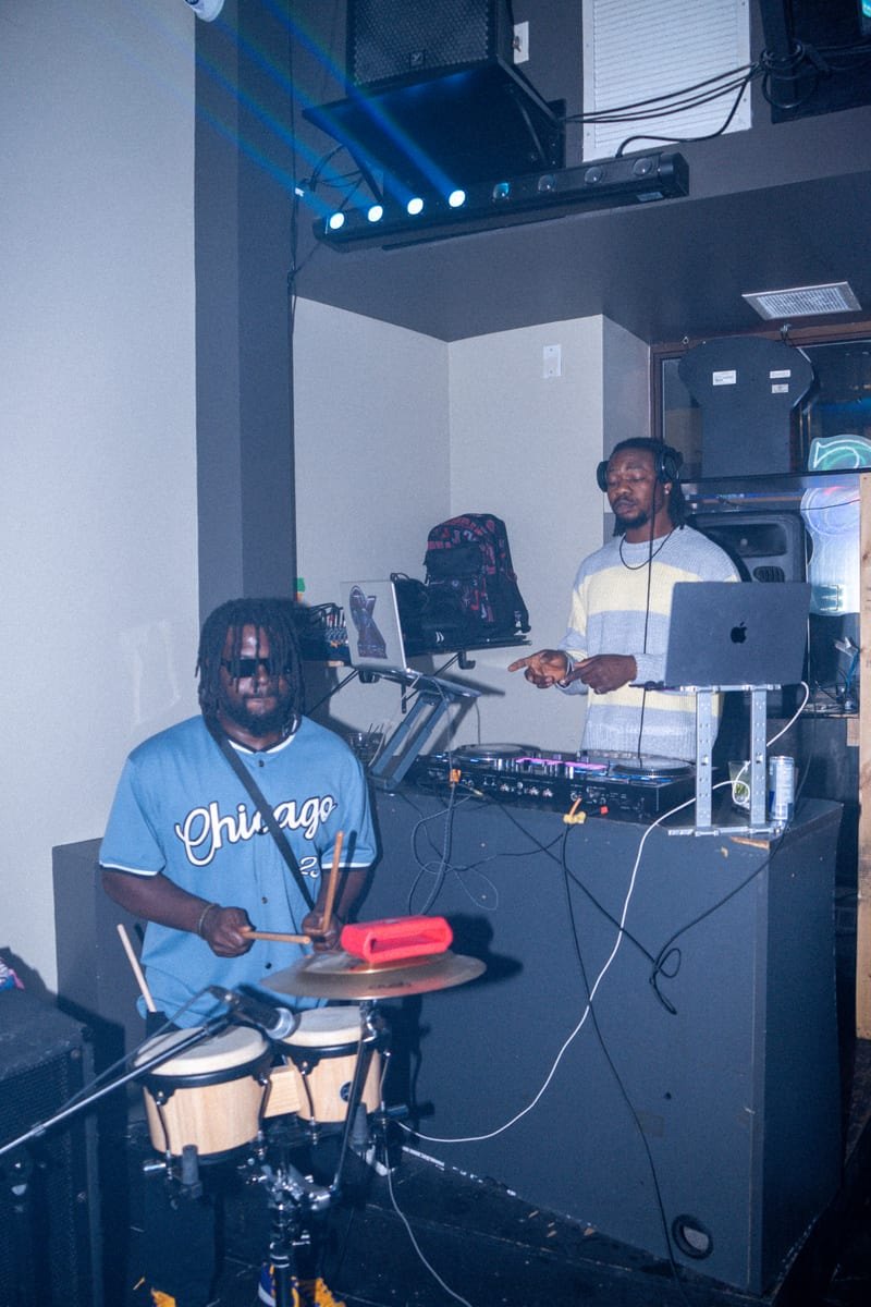 DJ at the decks with a percussionist in a Chicago jersey playing congas beside him