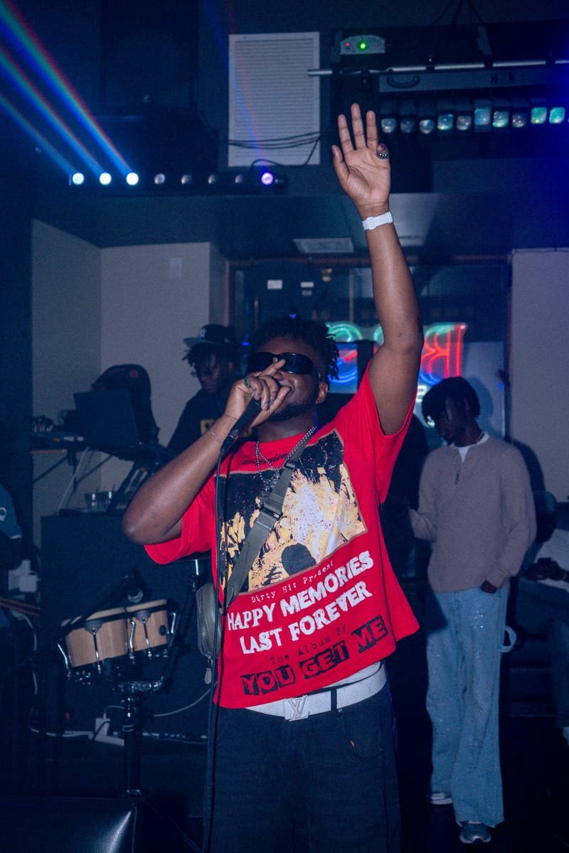 Performer in a red tee with an arm raised, blue stage lights behind him