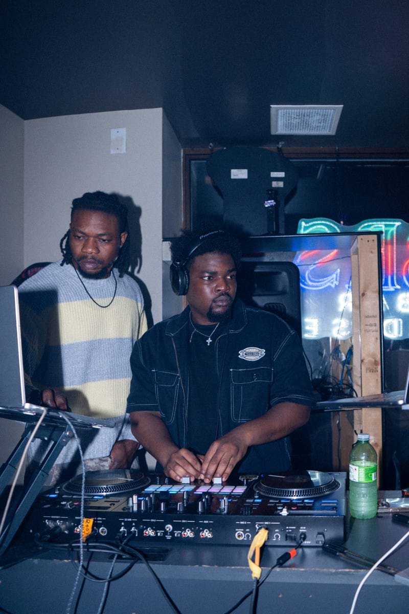 DJ with headphones at the decks and a second DJ beside him
