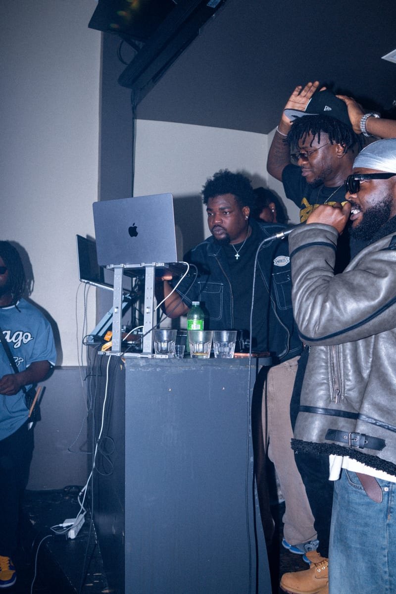 Artist with the mic at the DJ booth, surrounded by friends