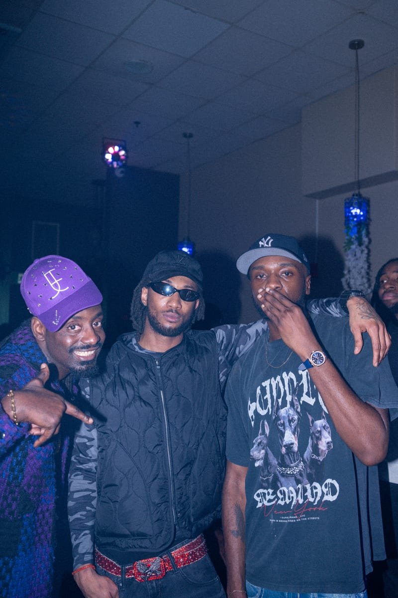 Three friends posing together, one in a purple cap