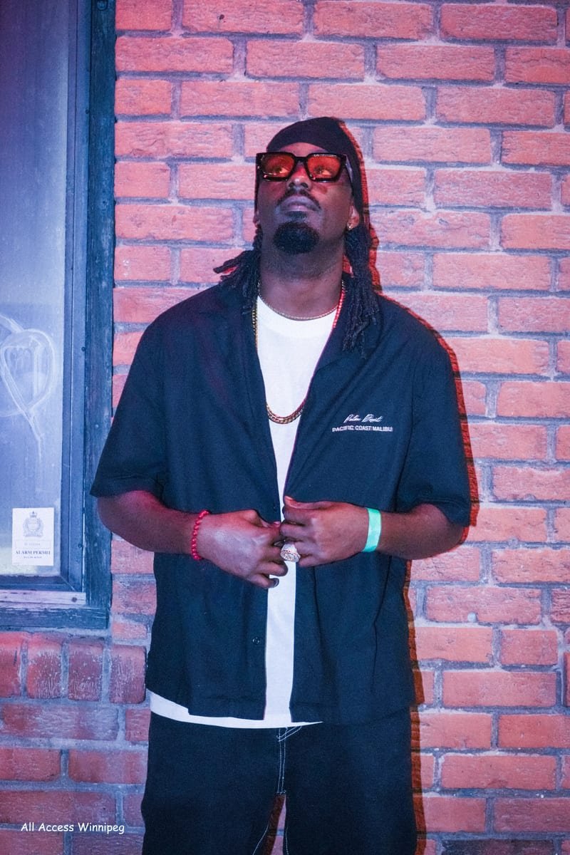 Artist portrait against a brick wall, sunglasses and chain