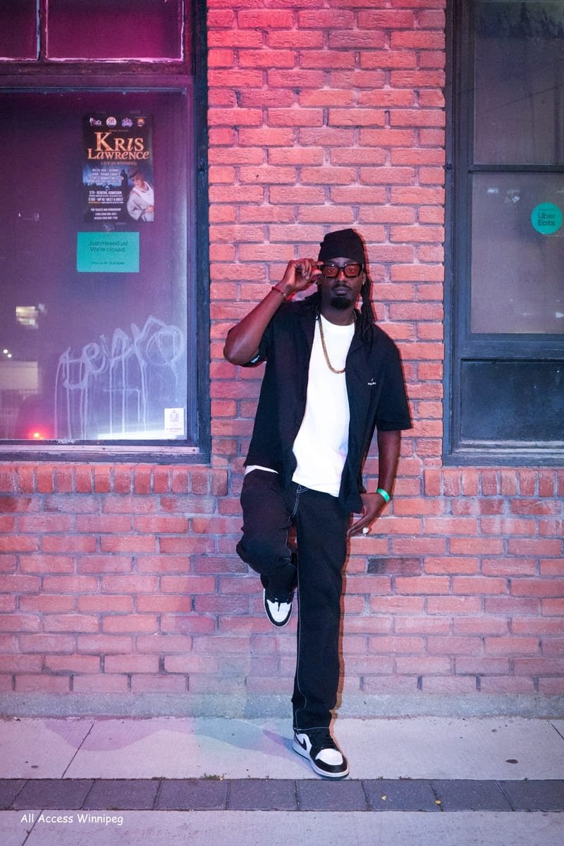 Artist leaning on a brick wall at night, hand raised
