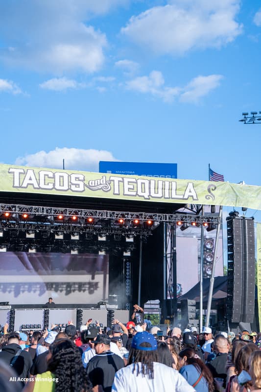 Wide shot of the main stage at dusk, crowd with hands up under the Tacos and Tequila banner