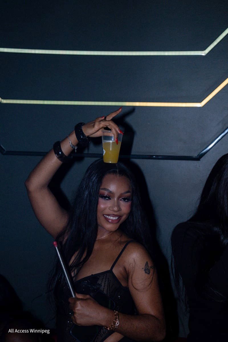 Guest smiling with a drink balanced on her head, cream neon lines behind her, VENTURA 2.0