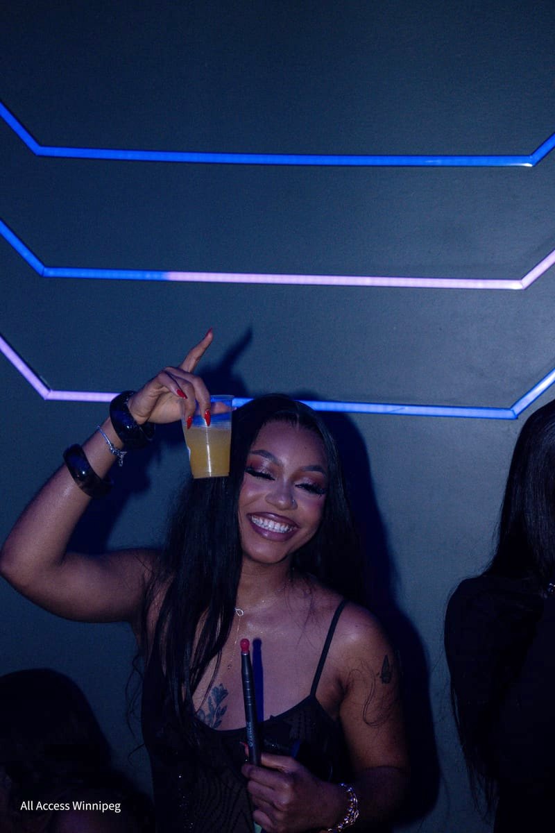 Guest smiling with a drink raised, blue neon lines behind her